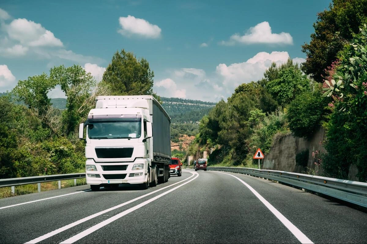 Freight Truck on Cross-Border Route Cargo truck driving along a tree-lined highway with other vehicles in the distance